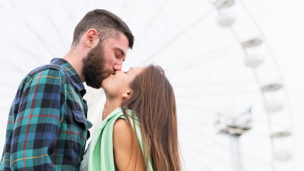 Vista lateral de casal se beijando ao ar livre