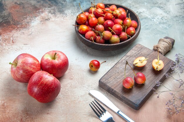 Vista lateral de close-up cerejas garfo faca cerejas na tigela e no quadro três maçãs