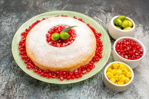 Vista lateral de close-up de bolo e doces um bolo e tigelas de sementes de romã doces de frutas cítricas