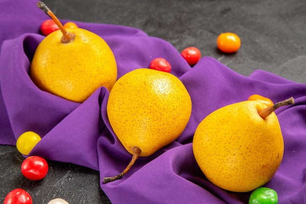 Vista lateral de close-up peras e doces doces coloridos peras meia pera na toalha roxa da mesa sobre a mesa
