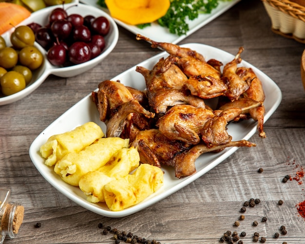 Vista lateral de codorna grelhada com lula kebab de batatas servidas com picles na mesa