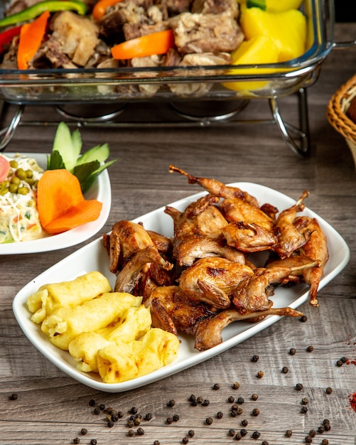 Vista lateral de codorna grelhada com lula kebab de batatas servidas com salada de legumes em cima da mesa