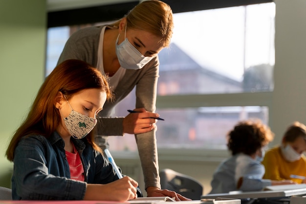 Foto grátis vista lateral de crianças aprendendo na escola com o professor durante a pandemia