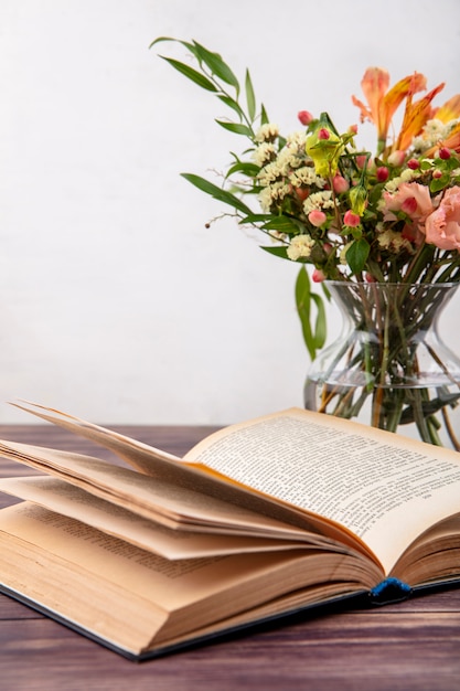 Vista lateral de diferentes flores brilhantes e maravilhosas com folhas em um vaso de vidro na superfície branca