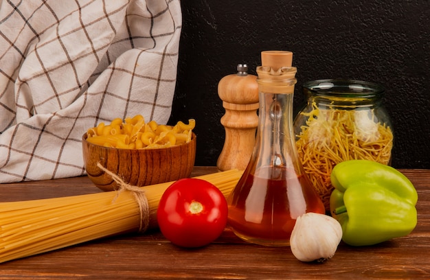 Vista lateral de diferentes macaronis com manteiga derretida tomate alho pimenta sal e pano xadrez na superfície de madeira e superfície preta