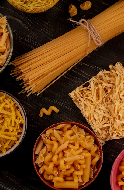 Vista lateral de diferentes tipos de macarrão como espaguete vermicelli tagliatelle e outros na mesa de madeira