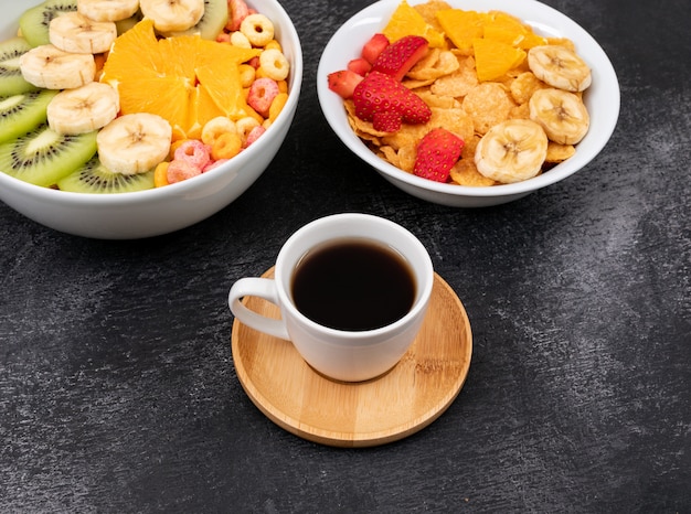 Vista lateral de flocos de milho com frutas e café na superfície preta horizontal