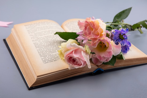 Vista lateral de flores em livro aberto em fundo cinza