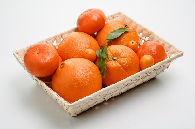 Vista lateral de frutas cítricas como laranja e kumquats na cesta em fundo branco