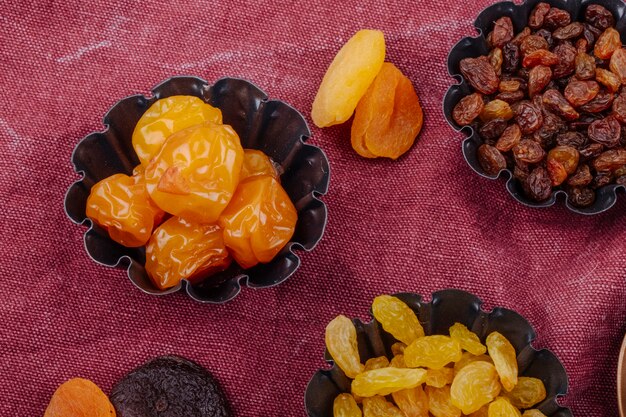 Vista lateral de frutas secas, ameixas de cereja, passas e damascos em latas de torta mini em fundo de textura de saco de carvão