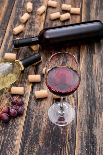 Foto grátis vista lateral de garrafas de vinho com vidro na vertical de madeira escura