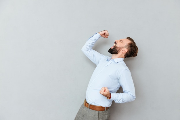 Vista lateral de gritar feliz homem barbudo em roupas de negócios