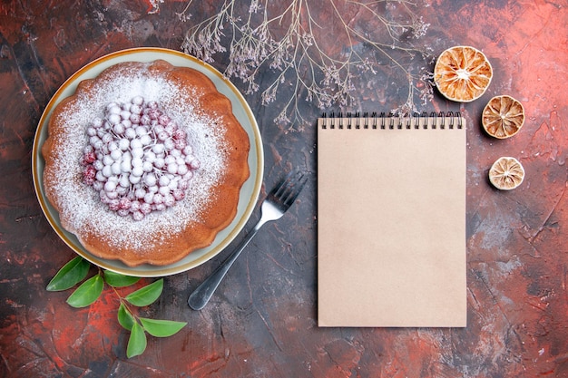 Vista lateral de longe um bolo um bolo com frutas silvestres folhas de limão creme caderno garfo na mesa