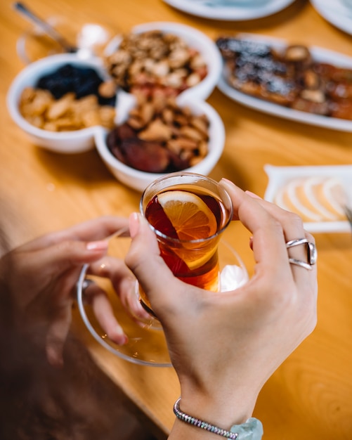 Vista lateral de mãos segurando um copo de armudu com chá preto