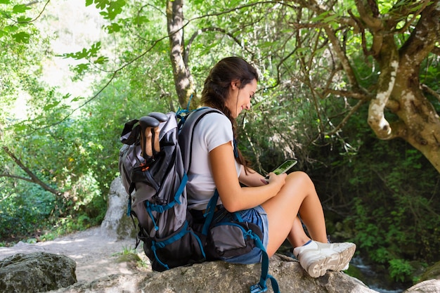 Foto grátis vista lateral de mulher com mochila olhando para o telefone enquanto explora a natureza