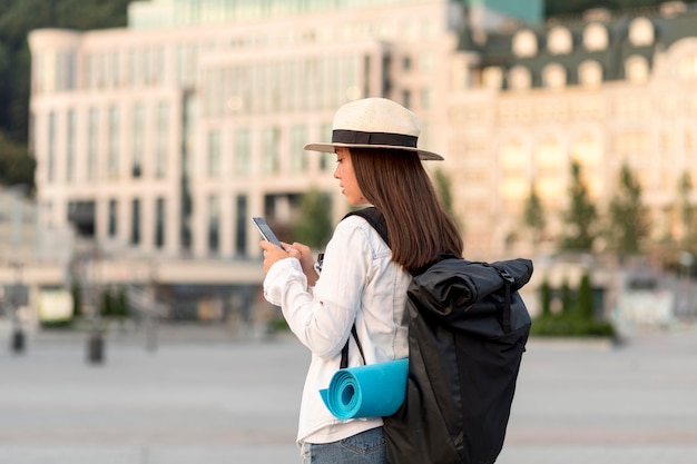 Vista lateral de mulher com smartphone viajando com mochila