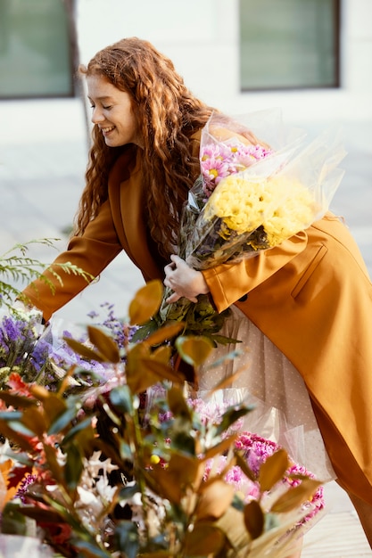 Vista lateral de mulher sorridente escolhendo buquê de flores de primavera