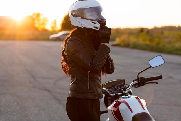 Vista lateral de mulher tirando o capacete ao lado da motocicleta