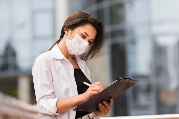 Vista lateral de mulher trabalhando durante a pandemia ao ar livre com o bloco de notas