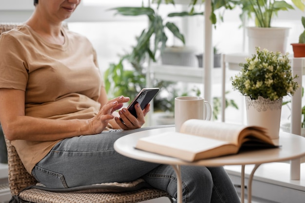 Foto grátis vista lateral de mulher usando smartphone dentro de casa