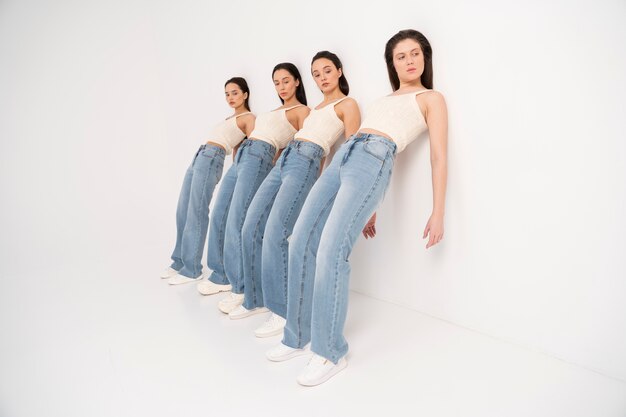 Vista lateral de mulheres em tops e jeans posando enquanto encostado na parede