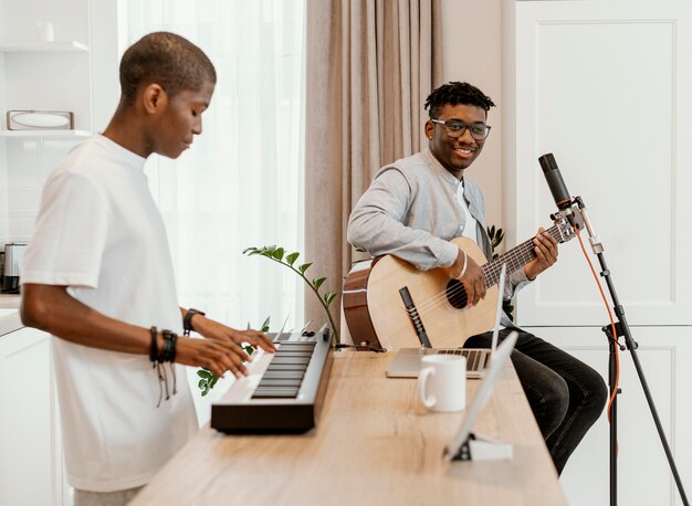 Vista lateral de músicos masculinos em casa tocando violão e teclado elétrico