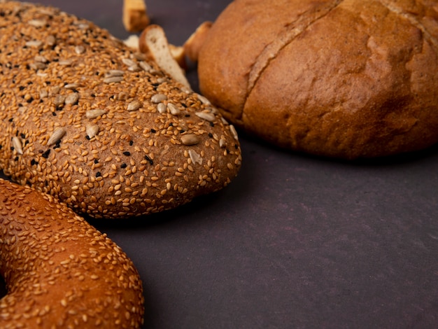 Vista lateral de pães como pão sanduíche de bagel e espiga clássica em fundo marrom com espaço de cópia