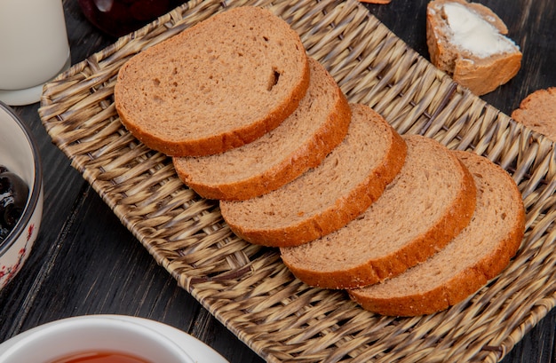 Vista lateral de pão de centeio fatiado no prato de cesta com azeite de oliva na mesa de madeira