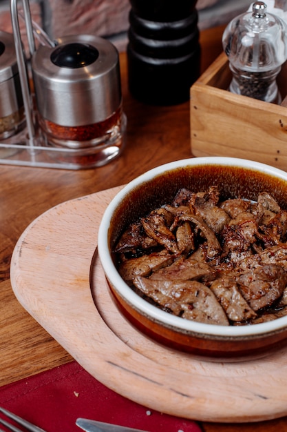 Foto grátis vista lateral de pedaços de carne frita em uma tigela de barro com especiarias em uma placa de madeira