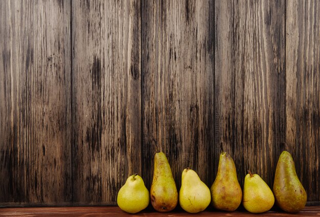 Vista lateral de peras maduras frescas em uma linha em um fundo de madeira com espaço de cópia