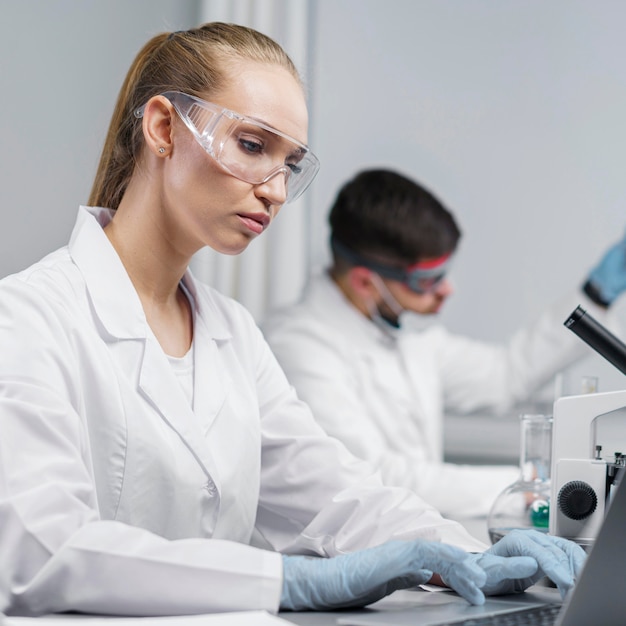 Vista lateral de pesquisadora no laboratório com óculos de segurança