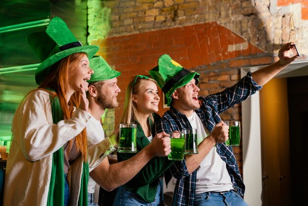 Vista lateral de pessoas felizes celebrando st. patrick's day e tirando selfie