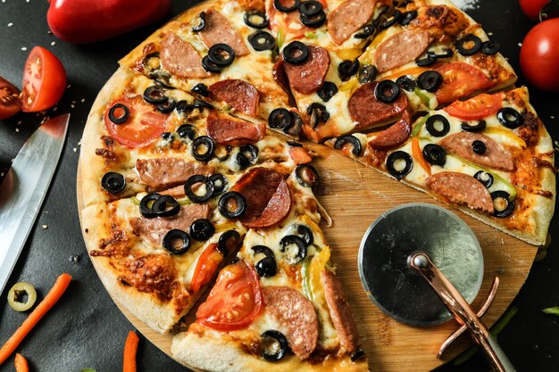 Vista lateral de pizza de salame em suporte com tomates, azeitonas e pimenta em mesa preta