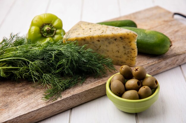 Vista lateral de queijo com pepino e pimentão em um suporte com azeitonas em um prato branco