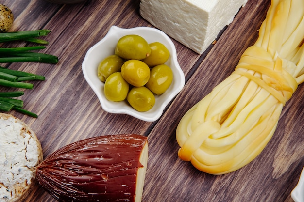 Vista lateral de queijo defumado e corda com azeitonas em conserva em madeira rústica