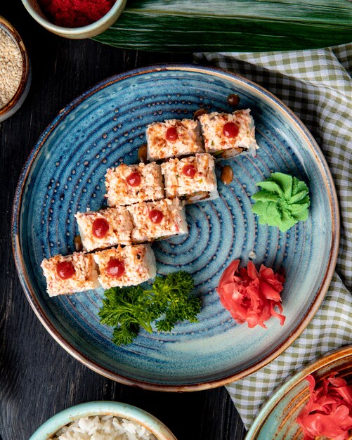 Vista lateral de rolos de sushi com arroz camarão tempura abacate e queijo dentro de um prato com gengibre e wasabi