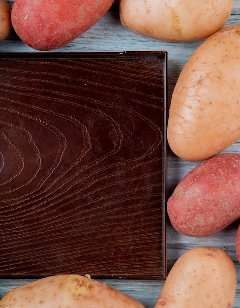 Vista lateral de russet e batatas vermelhas, situado em forma quadrada em torno da bandeja vazia na mesa de madeira
