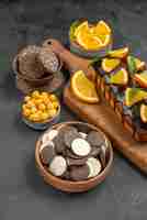 Foto grátis vista lateral de saborosos bolos cortados em laranjas com biscoitos na tábua de cortar na mesa escura