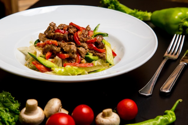 Vista lateral de salada quente com carne e legumes com cogumelos e tomates