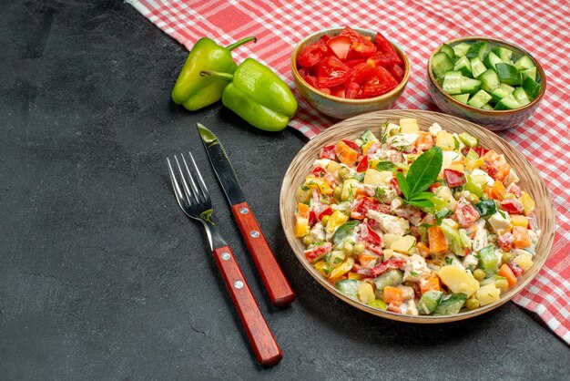 Vista lateral de salada vegetariana com legumes e talheres ao lado e guardanapo vermelho na mesa cinza
