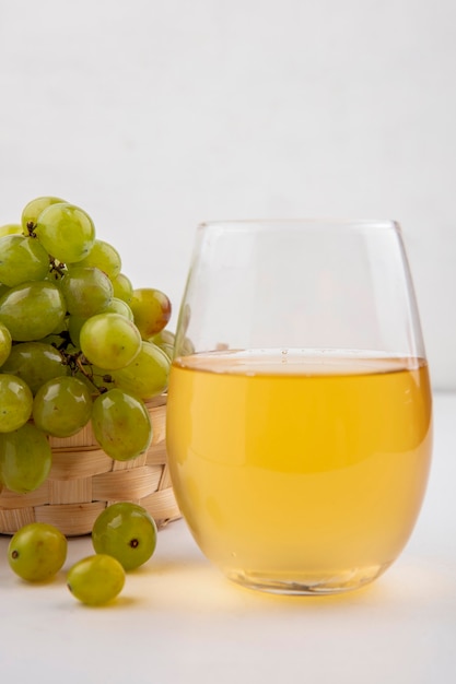 Vista lateral de suco de uva branca em um copo com uva branca na cesta no fundo branco