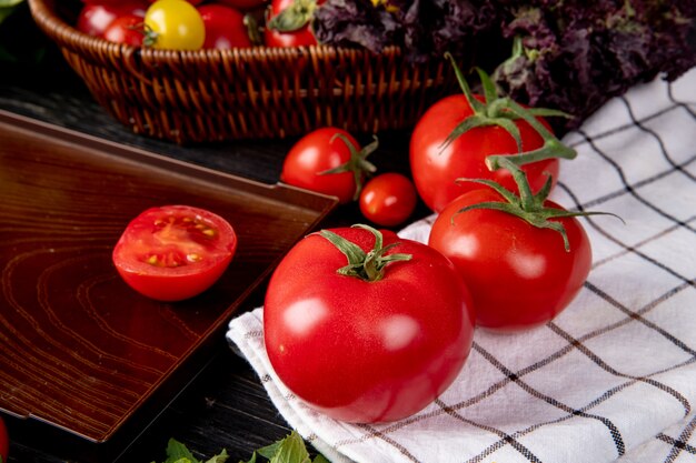 Vista lateral de tomate no pano xadrez e corte o tomate na bandeja na mesa de madeira