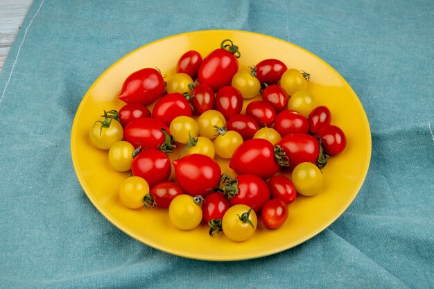 Vista lateral de tomates amarelos e vermelhos no prato na superfície de pano azul