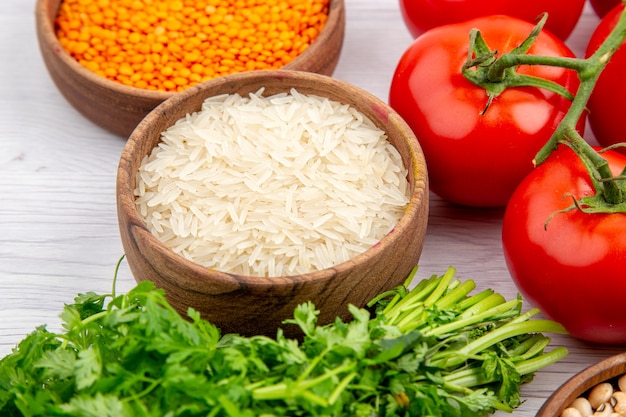 Vista lateral de tomates frescos com grãos de milho caule, arroz longo pacote de verduras na mesa branca