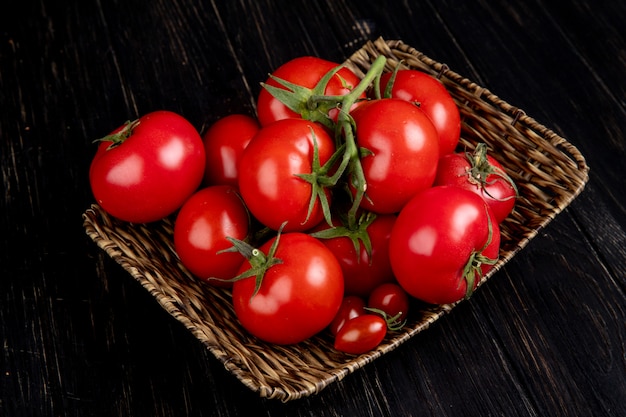 Vista lateral de tomates no prato de cesta na mesa de madeira