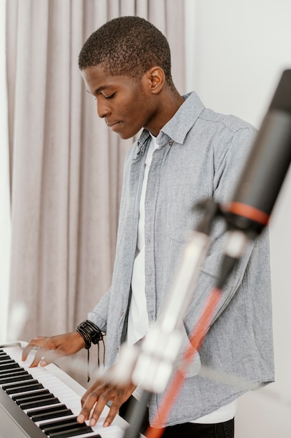 Vista lateral de um belo músico masculino em casa tocando teclado elétrico