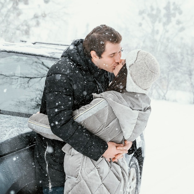 Vista lateral de um casal se beijando na neve durante uma viagem