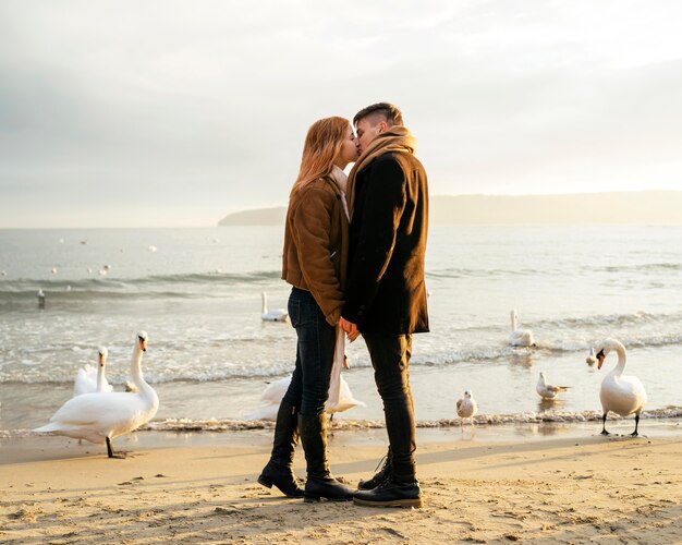 Vista lateral de um casal se beijando na praia no inverno