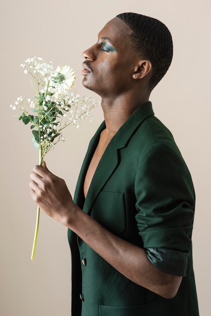Vista lateral de um homem bonito posando de blazer e se maquiando enquanto segura flores