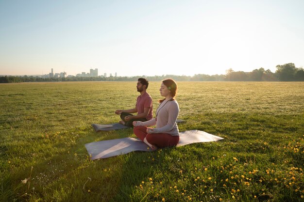 Vista lateral de um homem e uma mulher meditando ao ar livre em esteiras de ioga